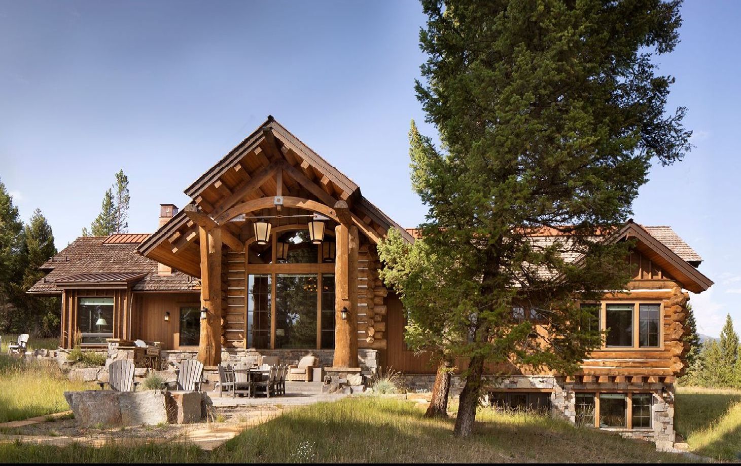 A large log cabin sits in the middle of a grassy field