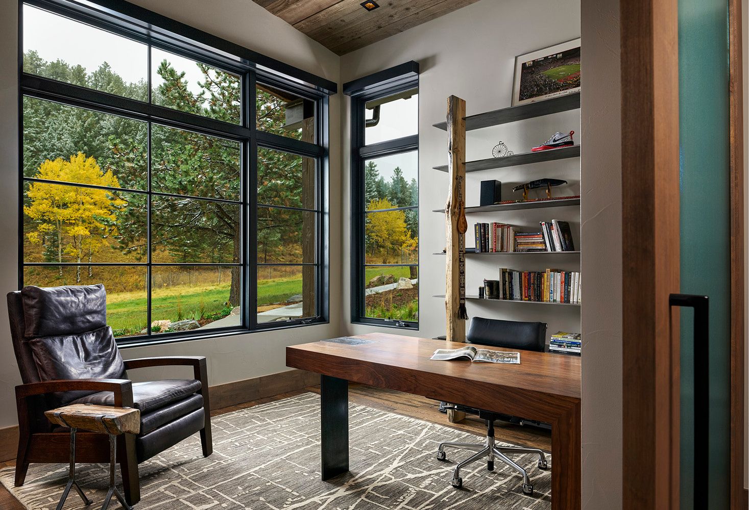 A home office with a desk , chair , bookshelf and large windows.