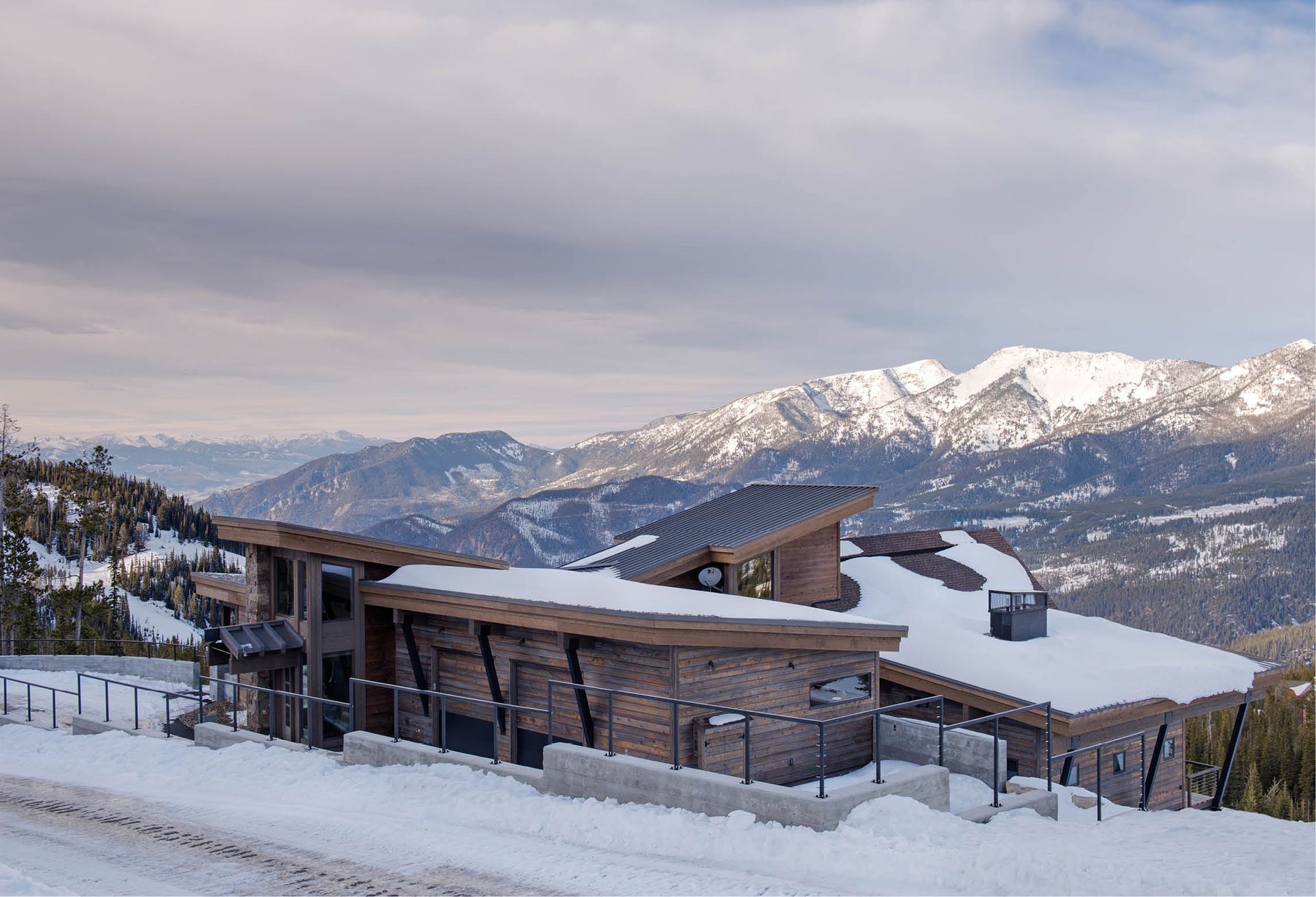 A house is sitting on top of a snow covered hill with mountains in the background.
