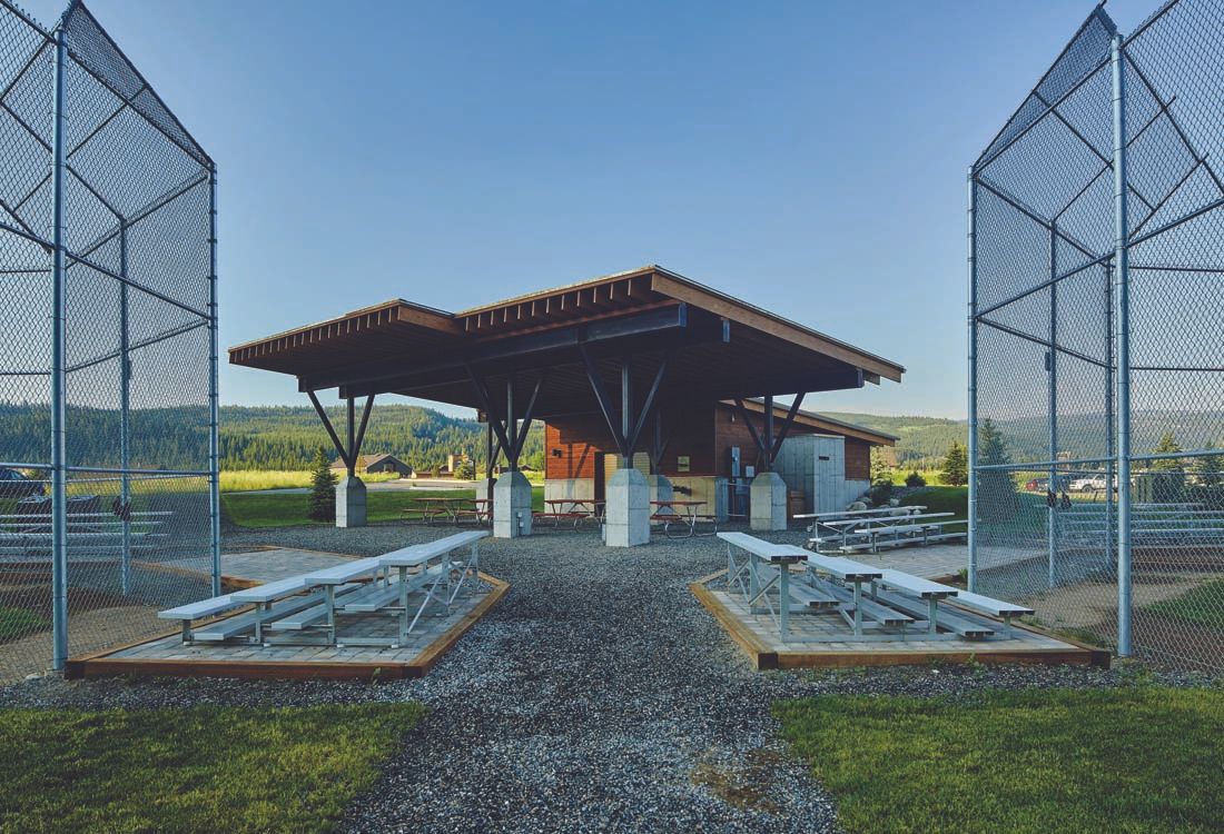 A fenced in area with picnic tables and a building in the background.