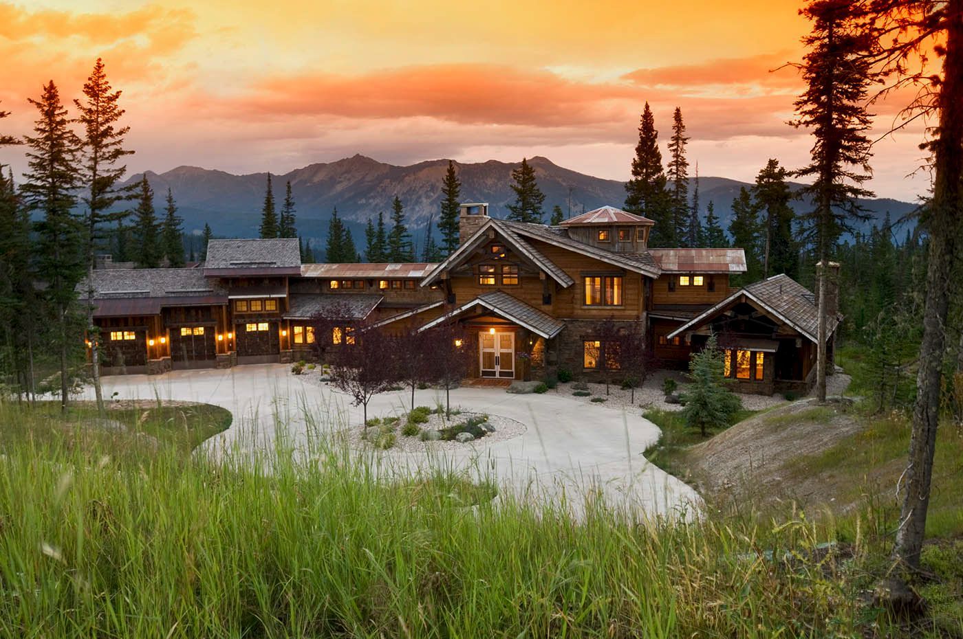 A large house is surrounded by trees and mountains at sunset.