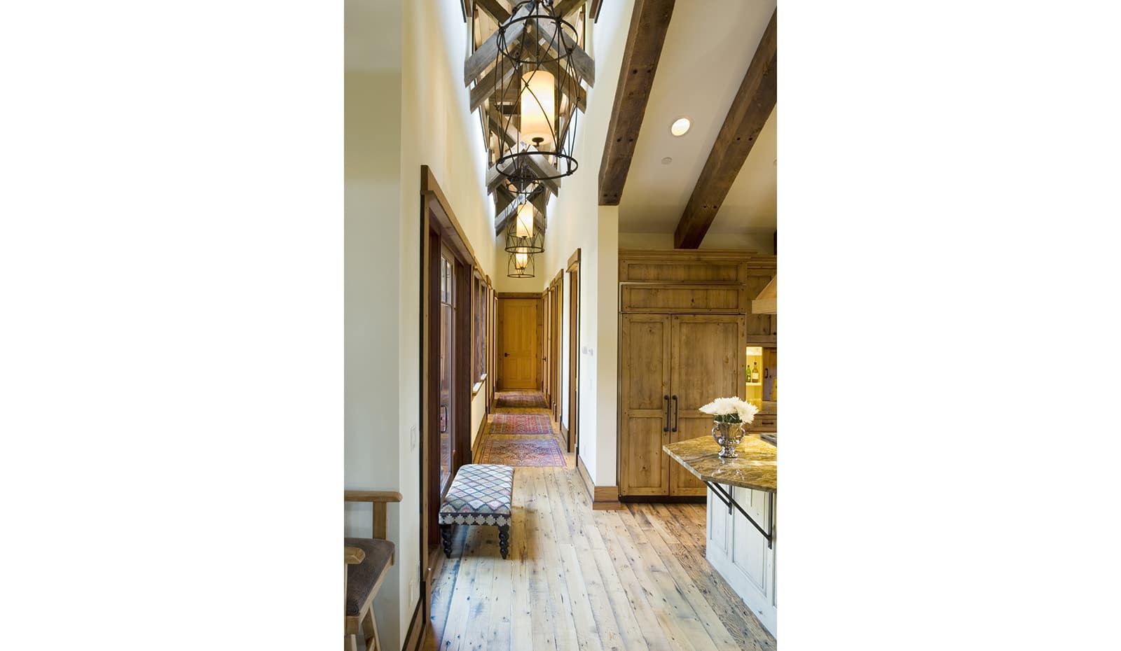 A long hallway in a house with a bench and a chandelier hanging from the ceiling.