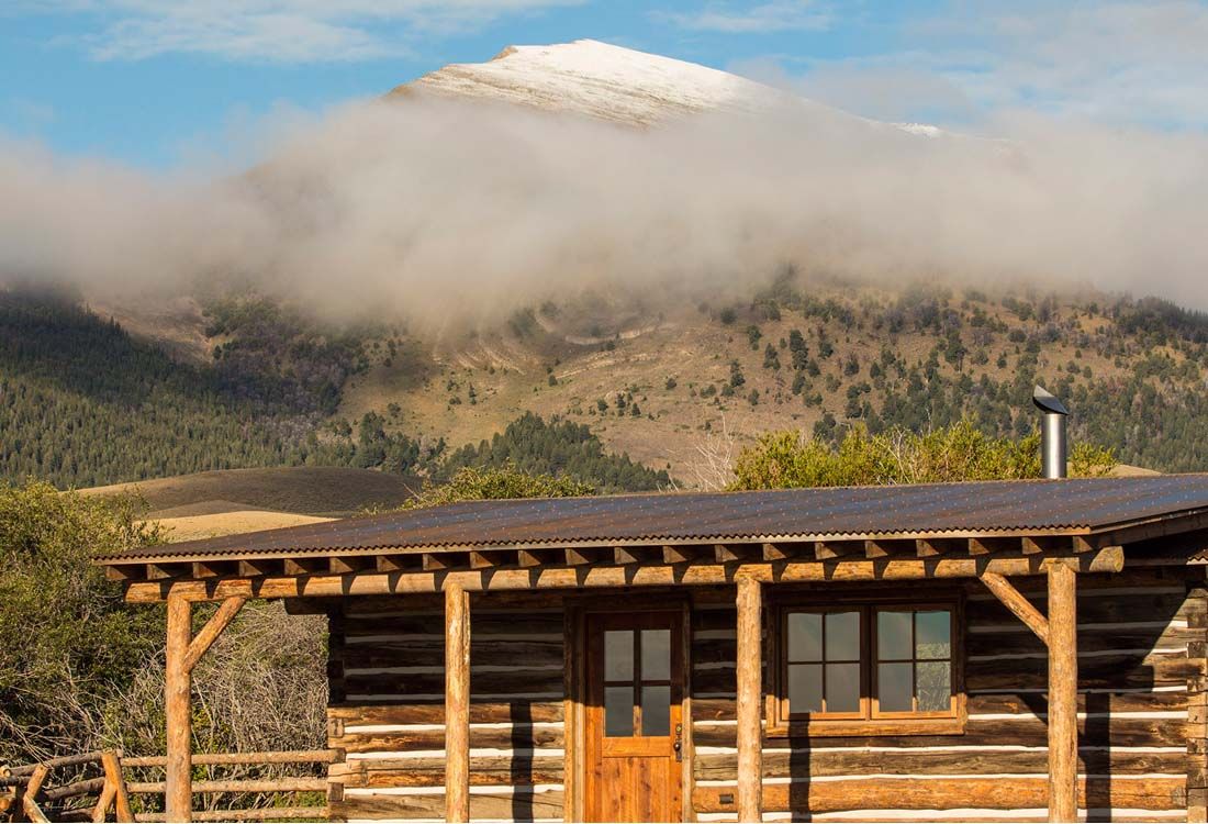 A log cabin in the mountains with a mountain in the background covered in clouds.