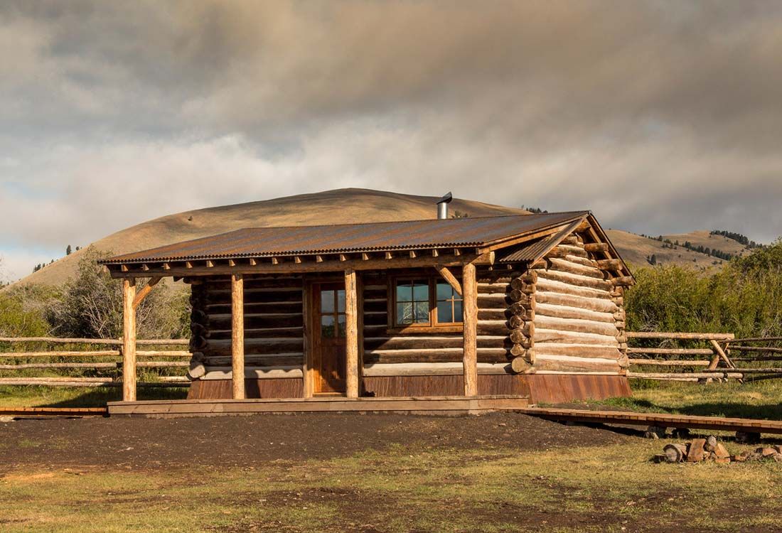 A small log cabin with a porch and a mountain in the background.