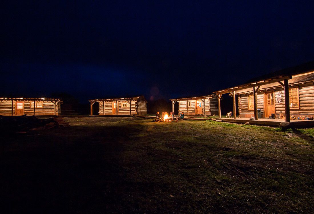A group of log cabins are lit up at night with a fire pit in the middle.