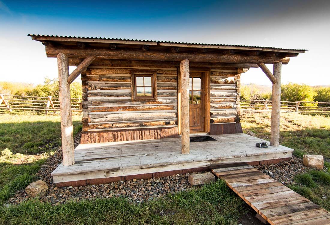 A small log cabin with a porch in the middle of a field.