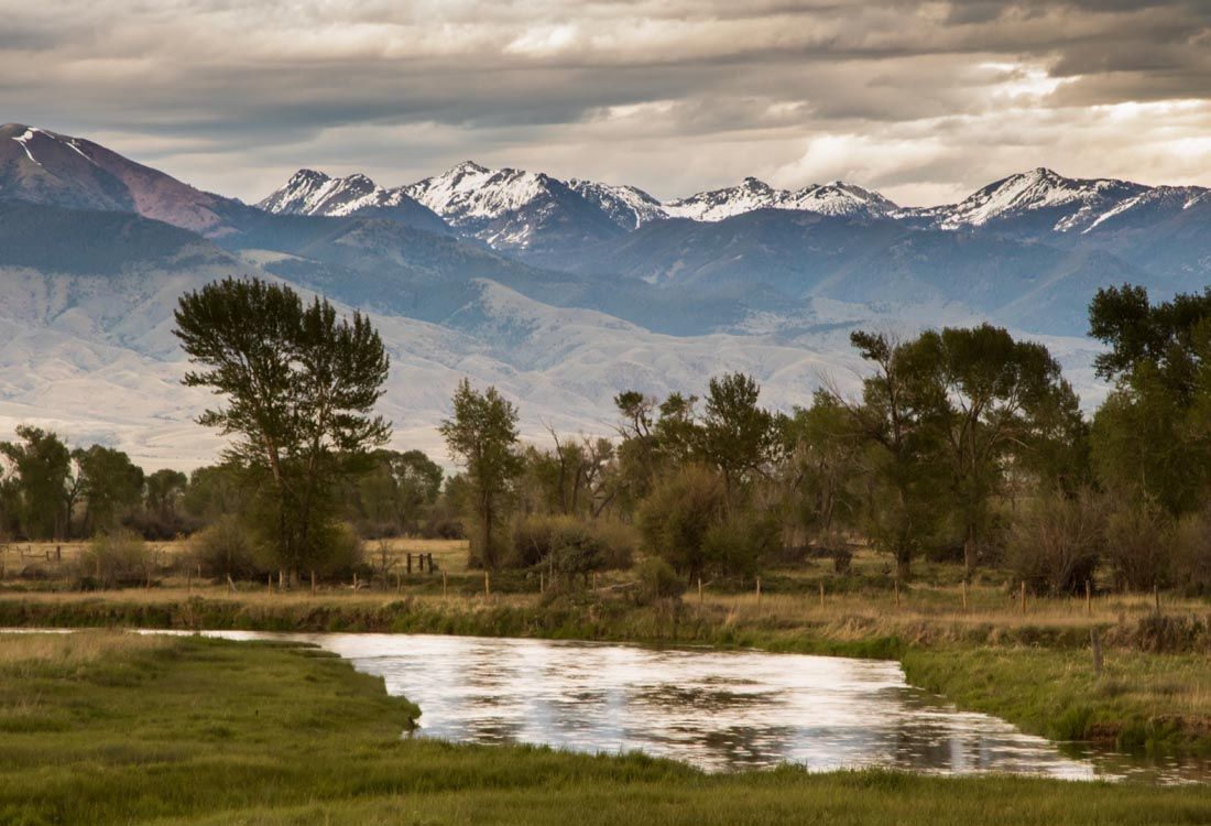 A river runs through a grassy field with mountains in the background.