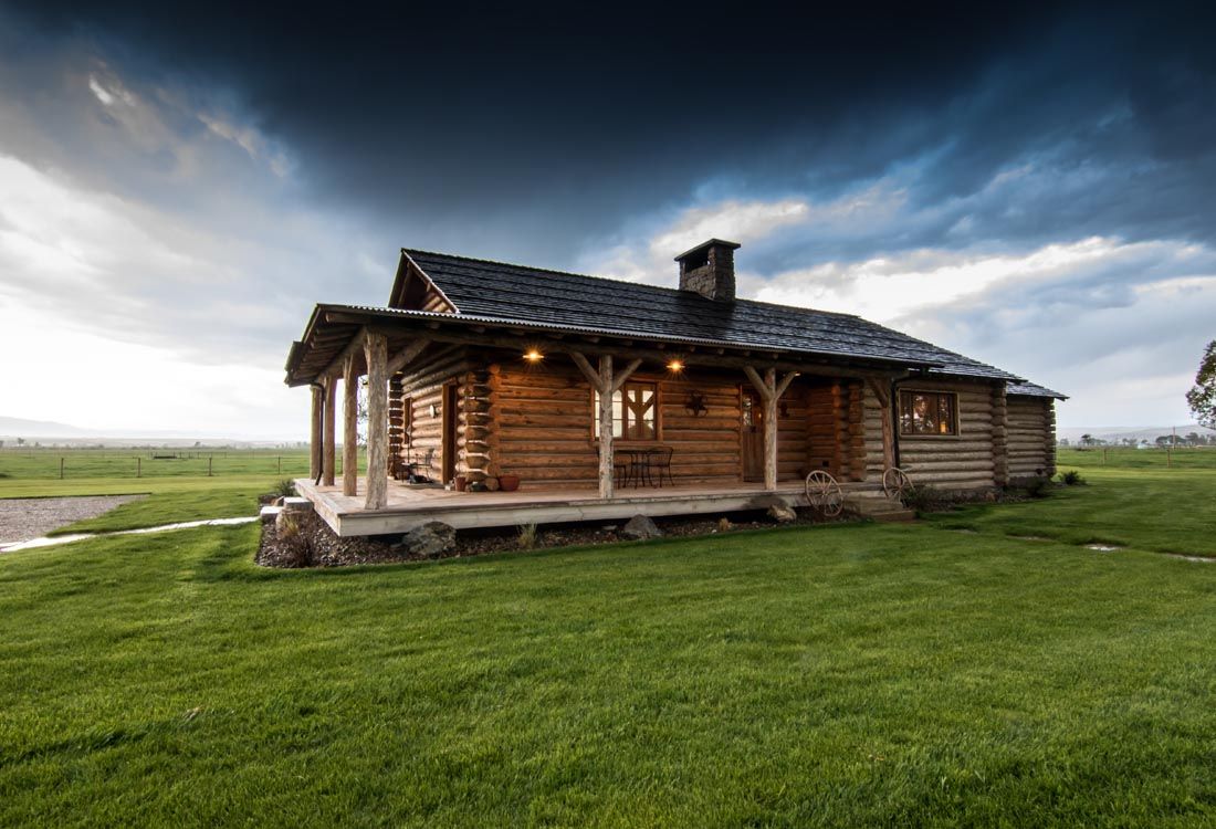 A log cabin with a porch in the middle of a grassy field.