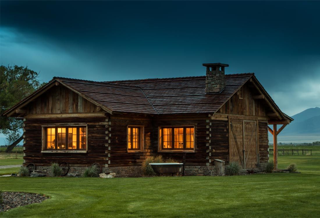 A log cabin is lit up at night in a grassy field.
