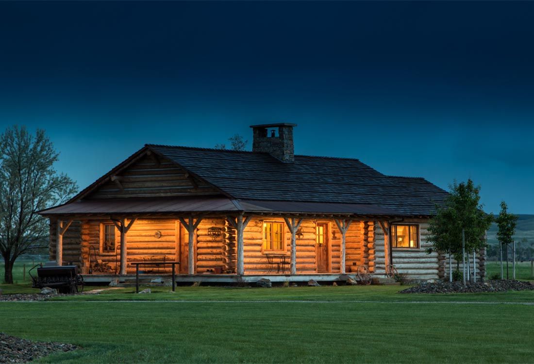 A log cabin is lit up at night in a grassy field.