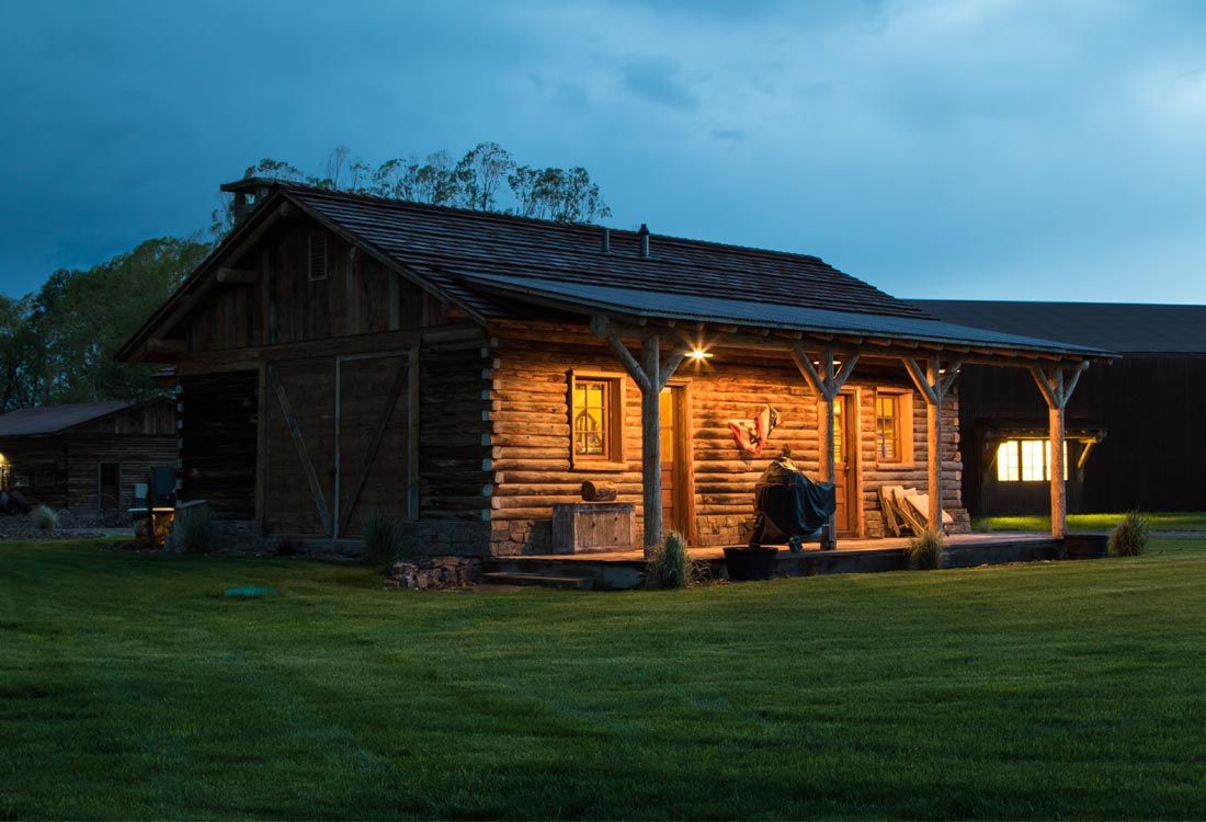 A log cabin with a porch is lit up at night.