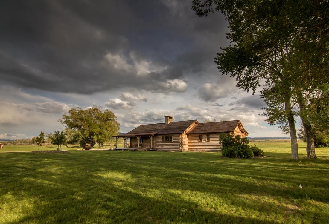 A log cabin is sitting in the middle of a grassy field under a cloudy sky.