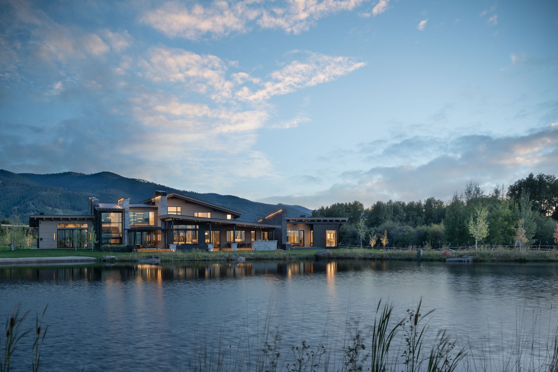 A large house is sitting next to a lake with mountains in the background.