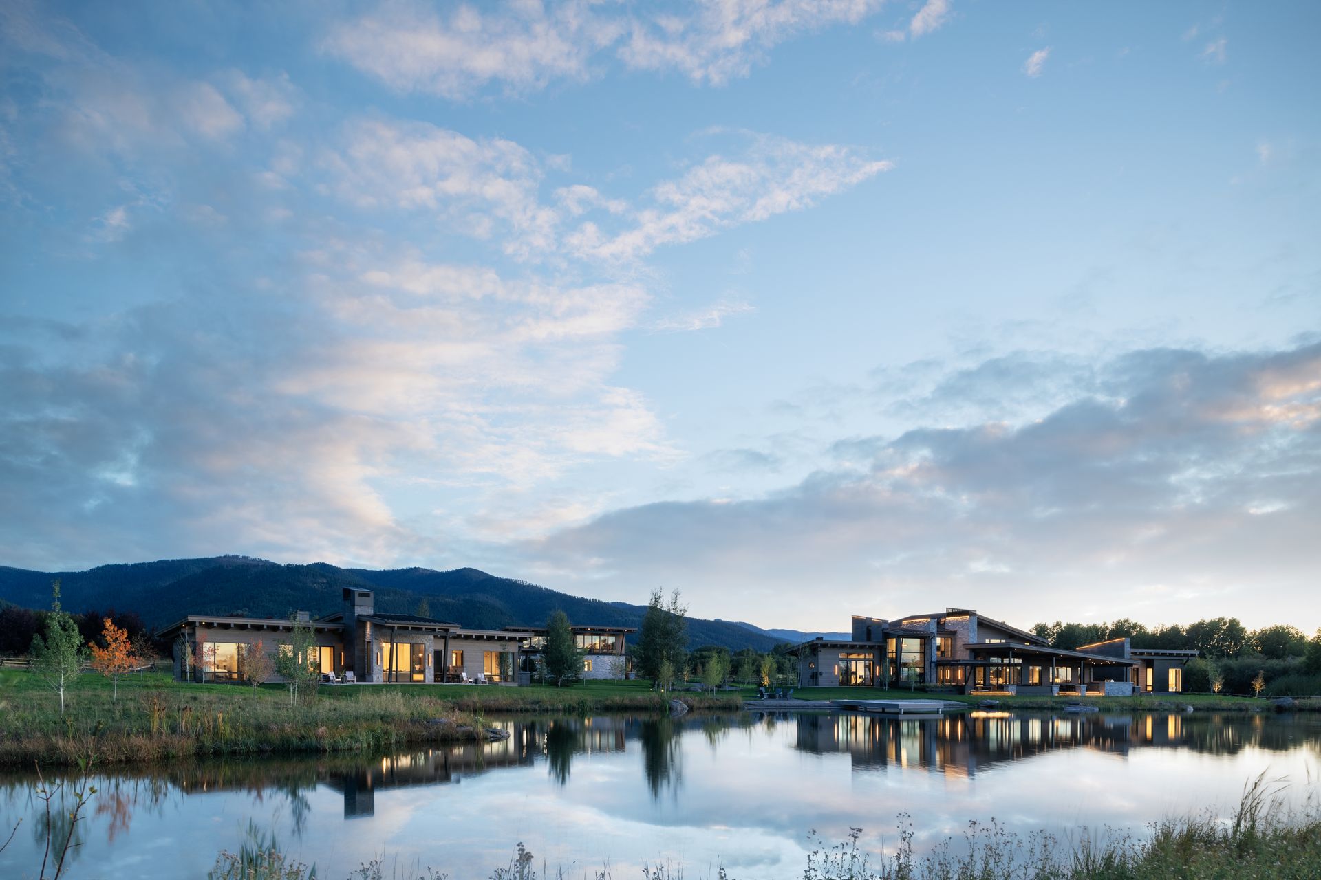 A large house is sitting next to a lake with mountains in the background.