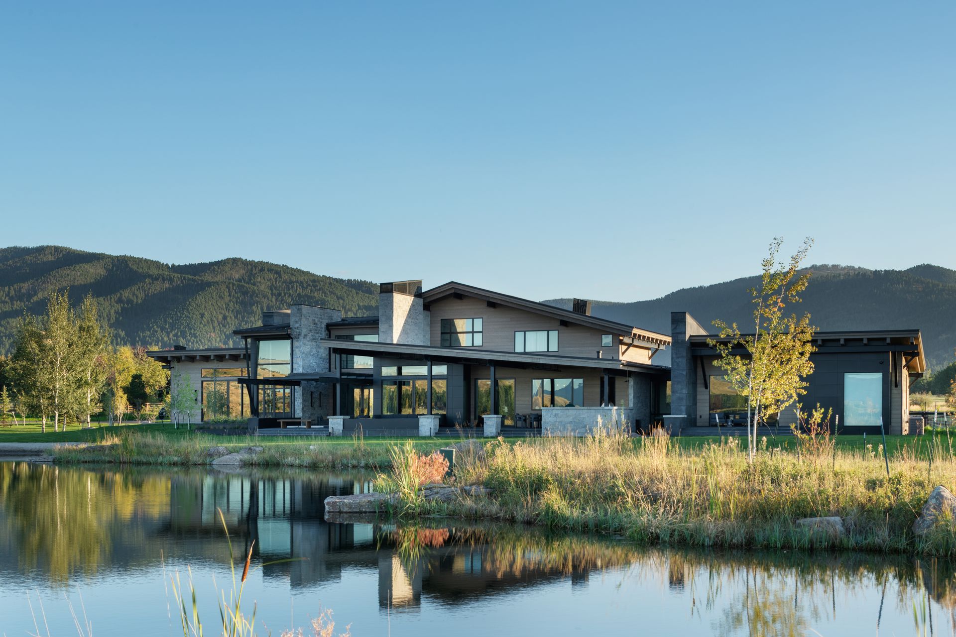 A large house is sitting next to a lake with mountains in the background.