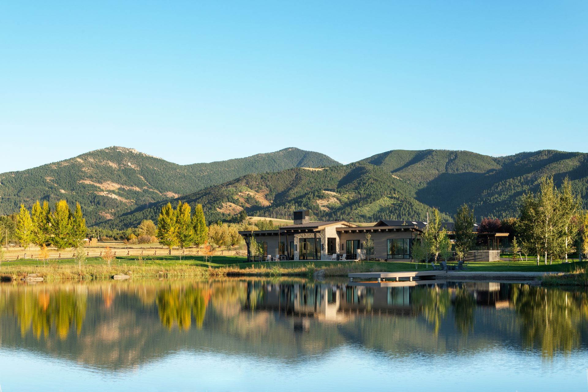 A house is sitting on the shore of a lake with mountains in the background.