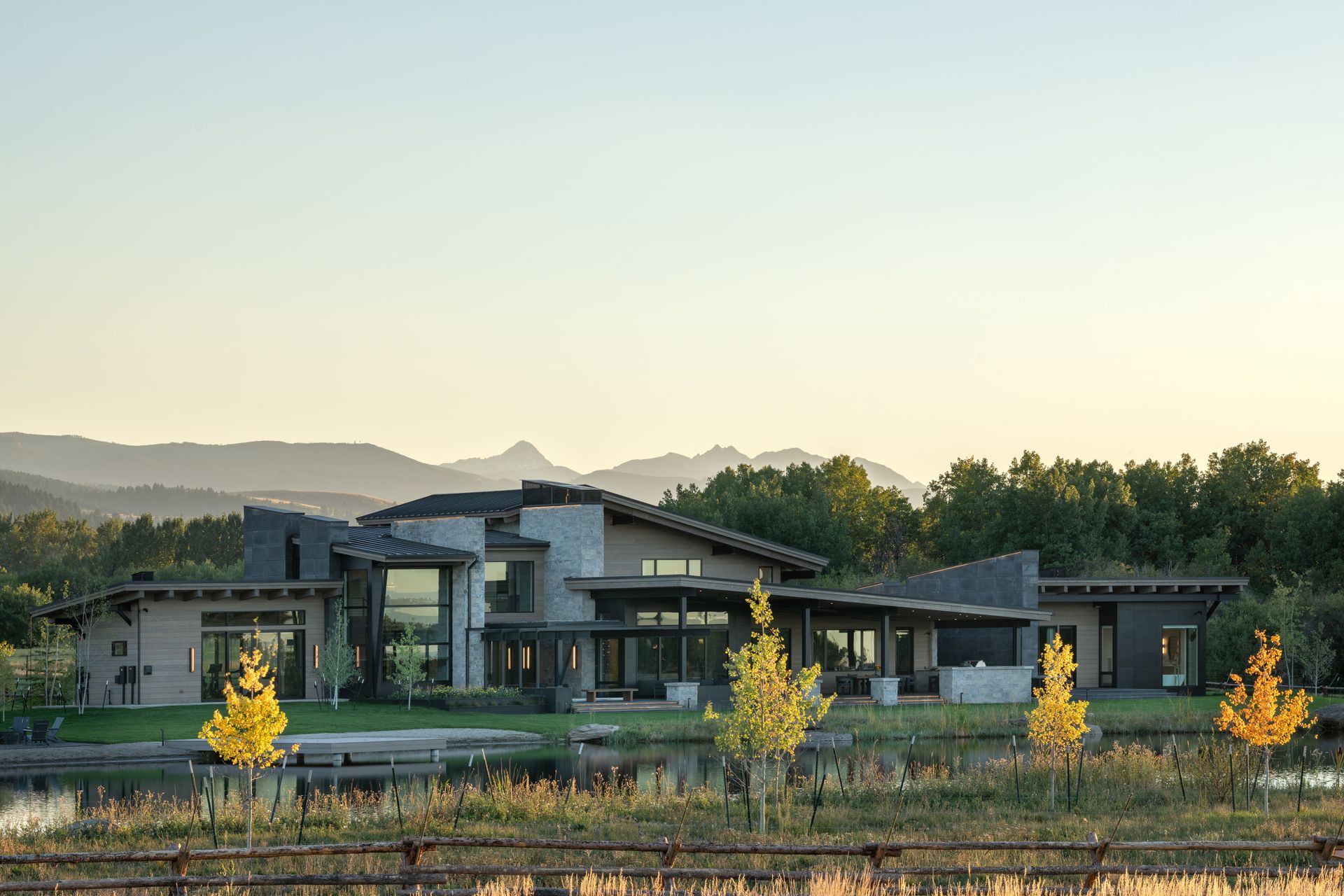 There is a large house in the middle of a field with mountains in the background.