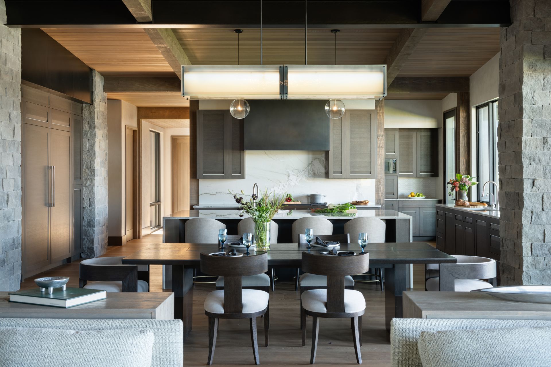 A dining room with a table and chairs and a kitchen in the background.