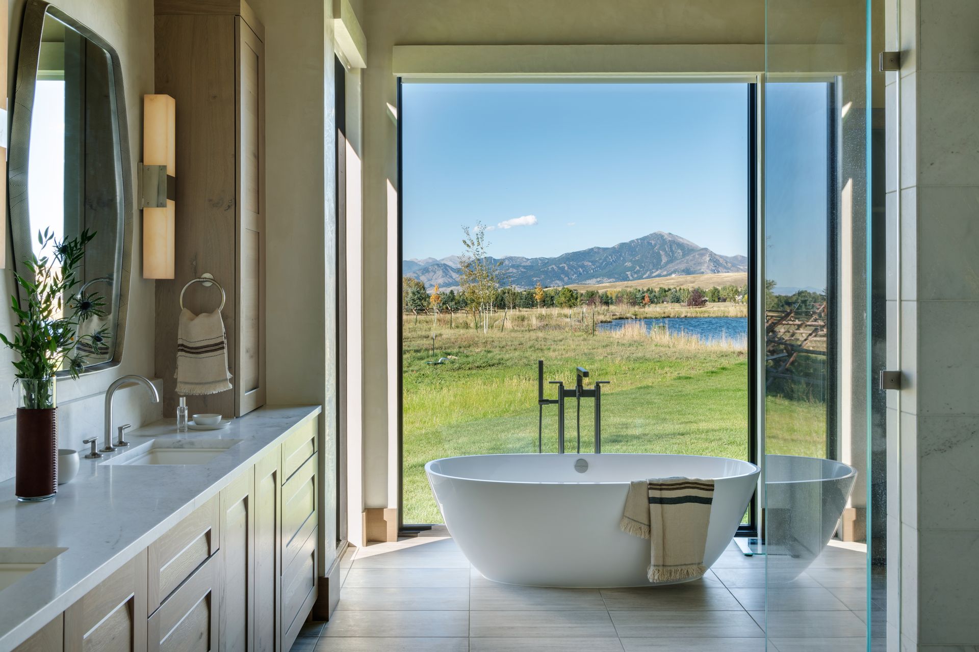 A bathroom with a tub , sink , mirror and large window.