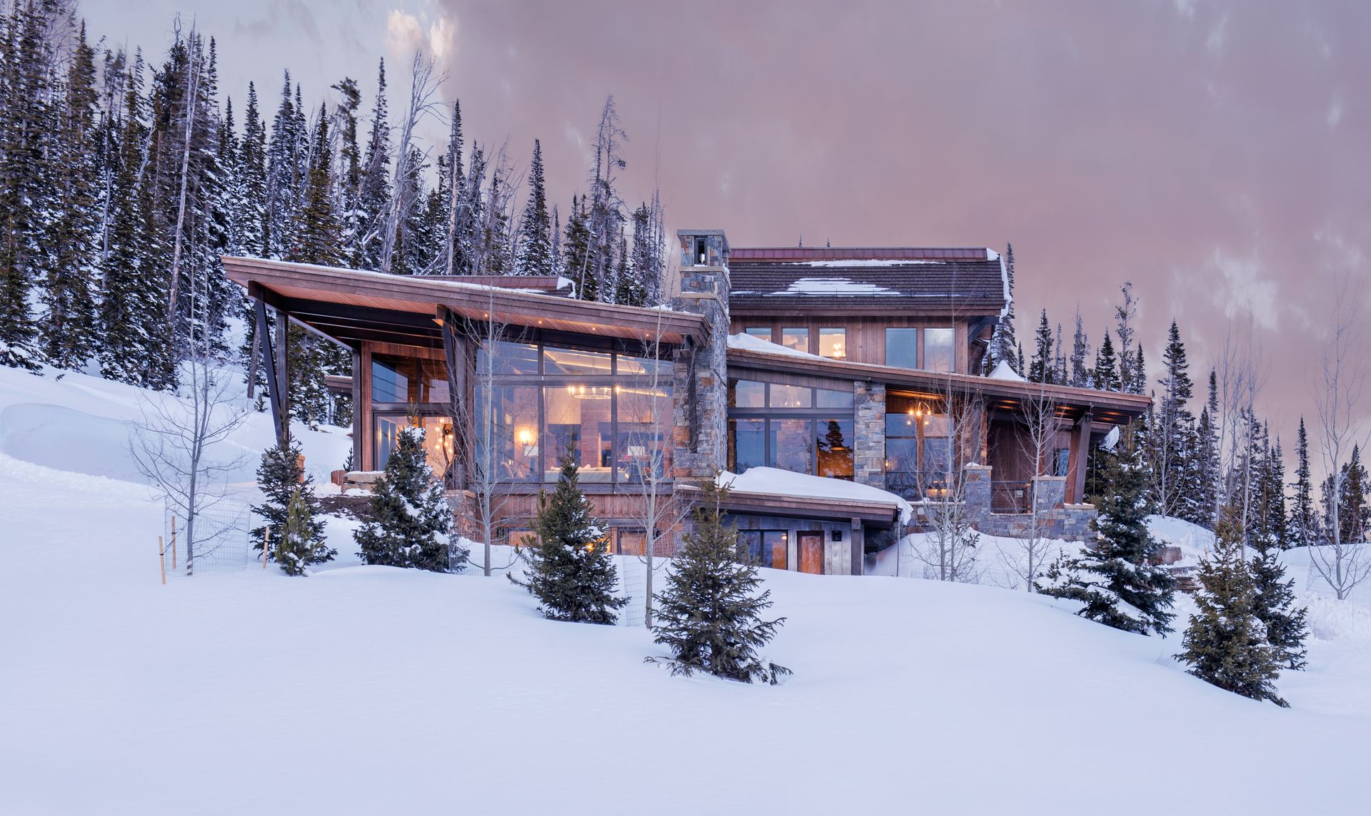 A large house is sitting on top of a snow covered hill surrounded by trees.