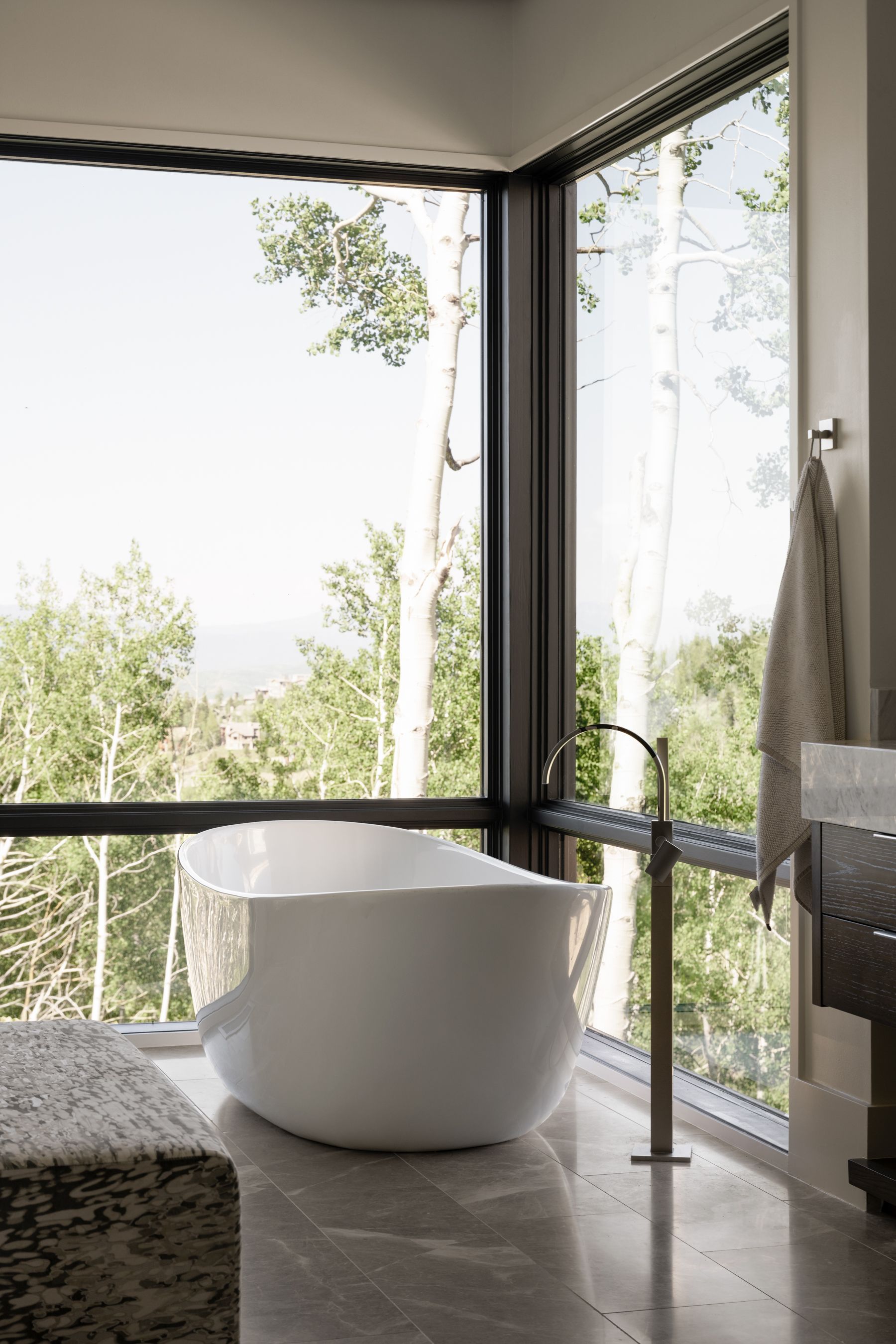 A bathroom with a tub and a large window with trees in the background.