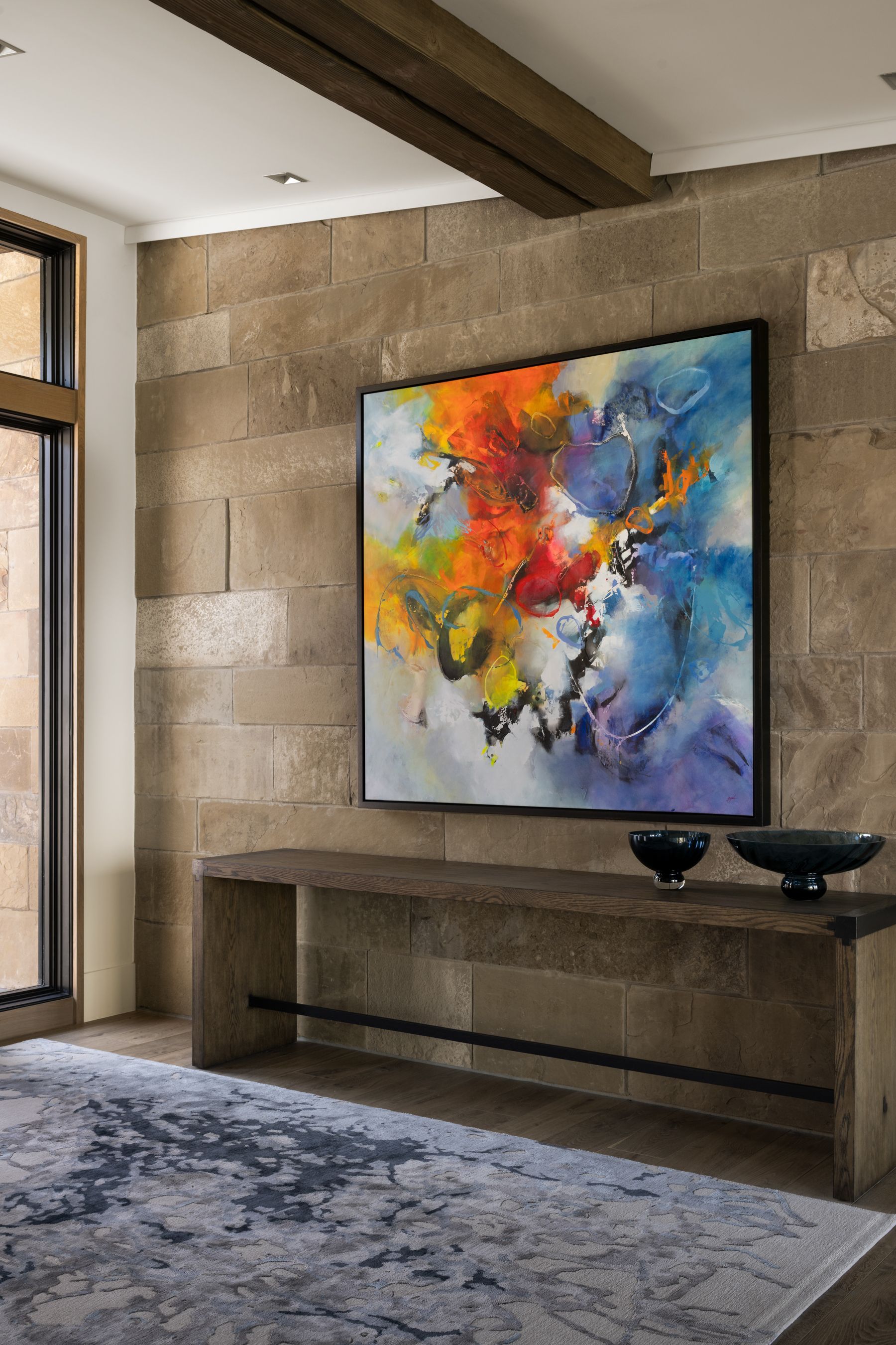A large painting is hanging on a wall above a table in a living room.