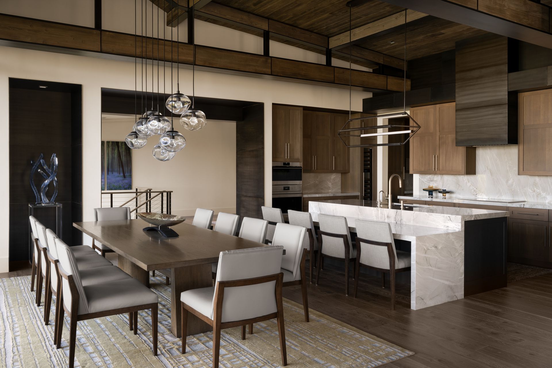 A dining room with a long table and chairs and a kitchen.