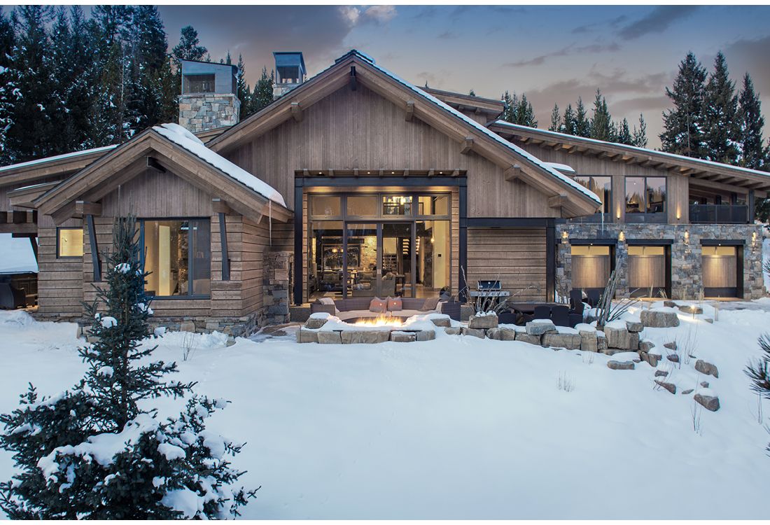 A large wooden house is surrounded by snow and trees.