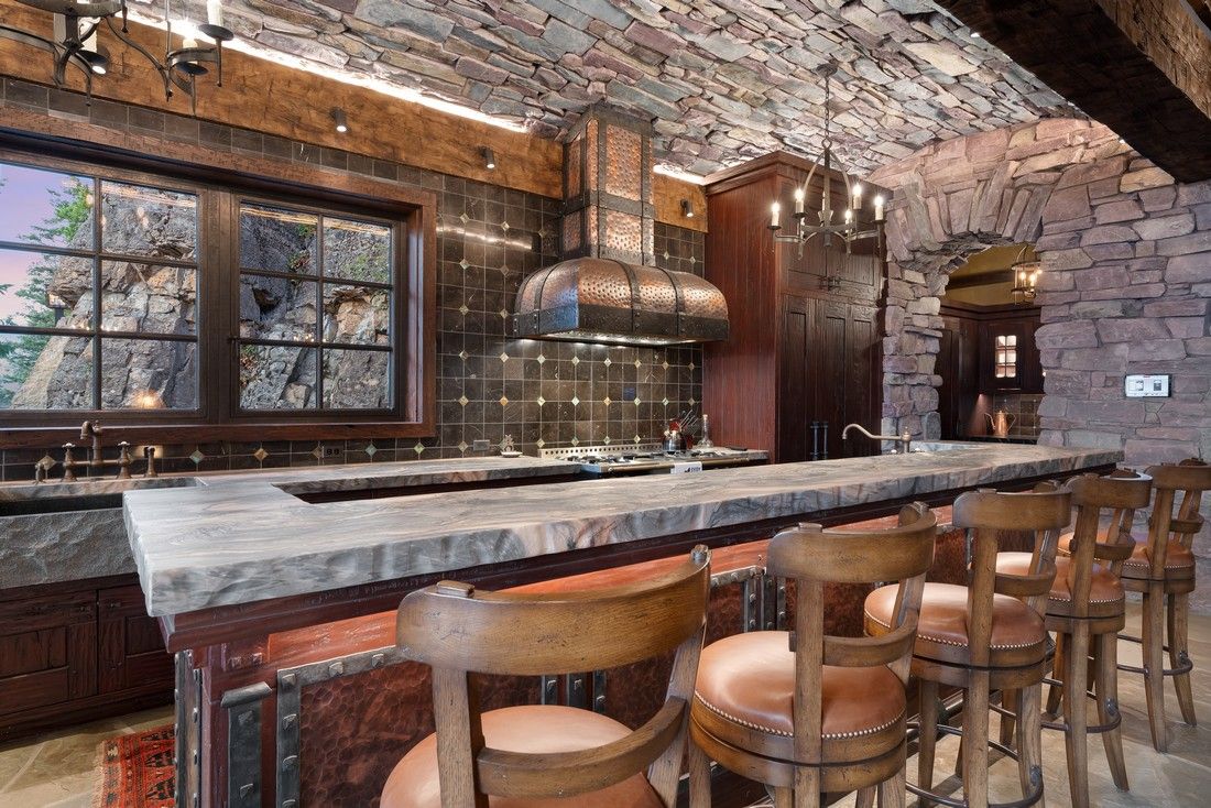 A kitchen with a long counter and chairs and a brick ceiling.