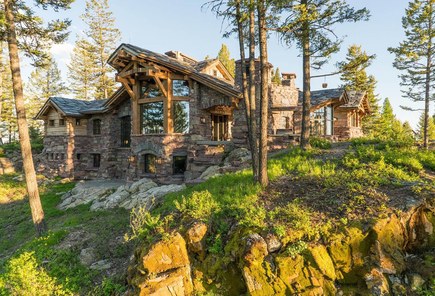 A large stone house is sitting on top of a rocky hill surrounded by trees.