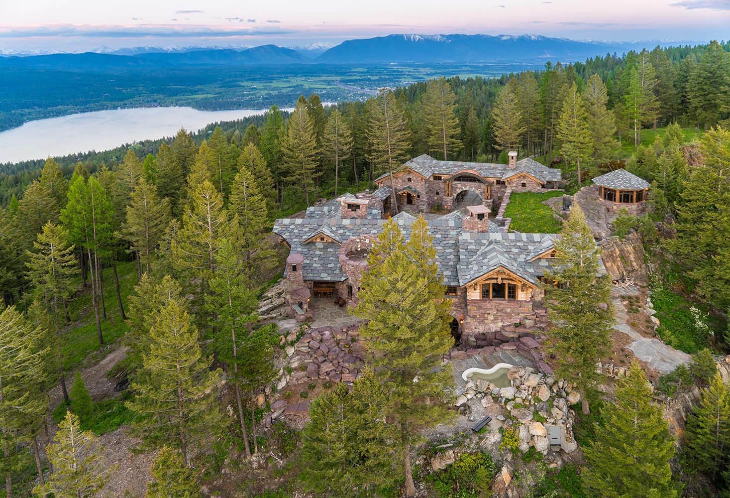 An aerial view of a large house surrounded by trees on top of a hill.