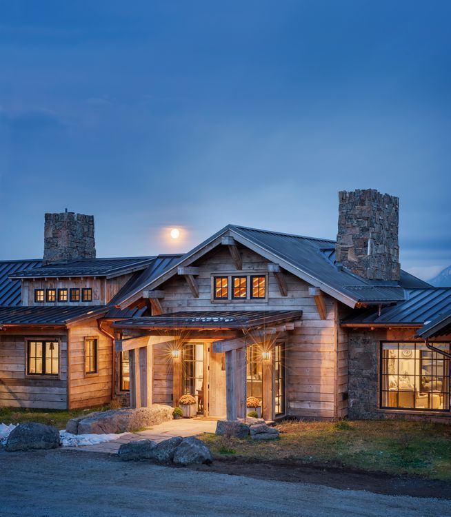 A large wooden house with a metal roof is lit up at night