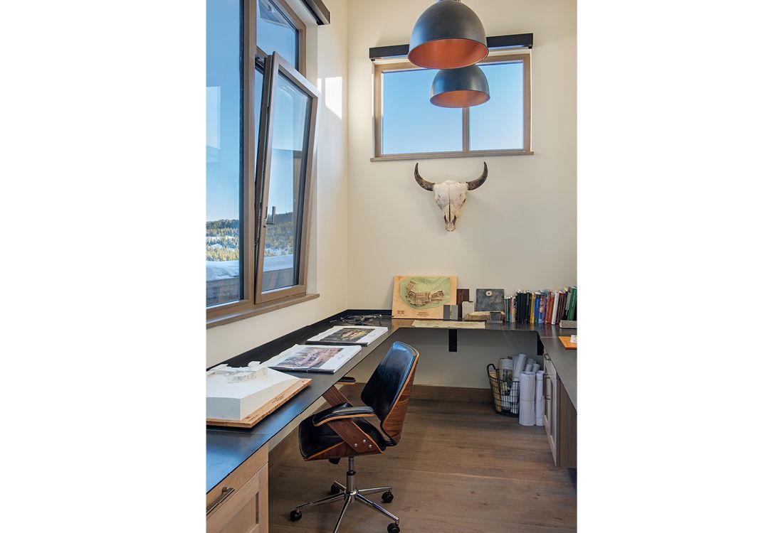A home office with a desk , chair , window and a bull skull on the wall.