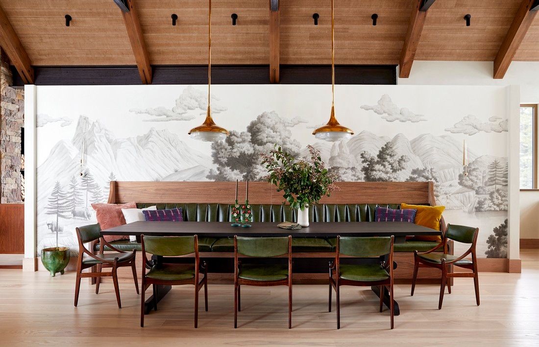 A dining room with a long table and chairs and a mural on the wall.