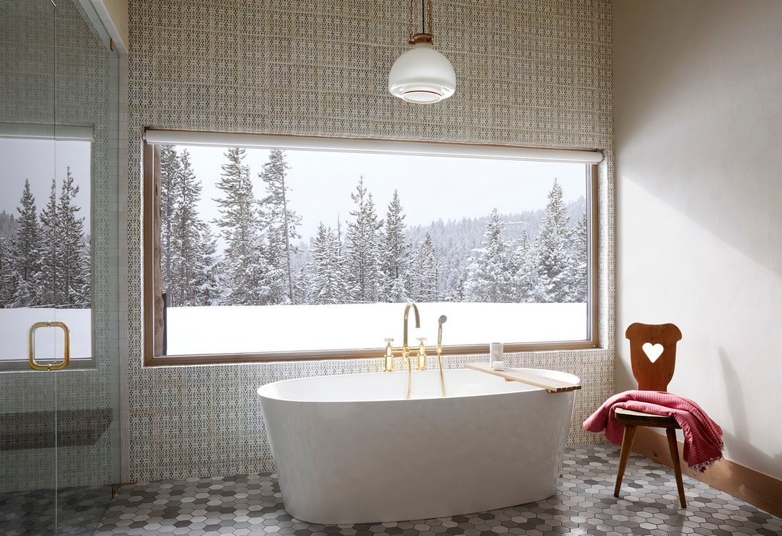 A bathroom with a tub and a window with a view of a snowy forest.