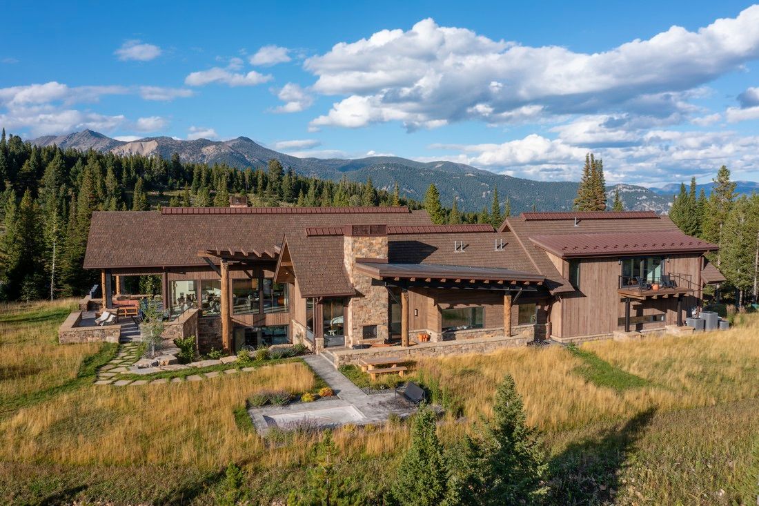 A large house is sitting in the middle of a field with mountains in the background.