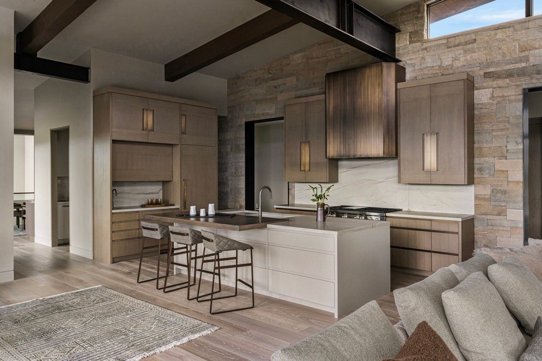 A kitchen with a large island and stools in a living room.
