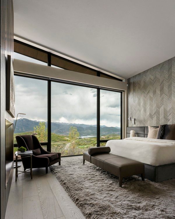 A bedroom with a large bed , chair , bench and large windows.