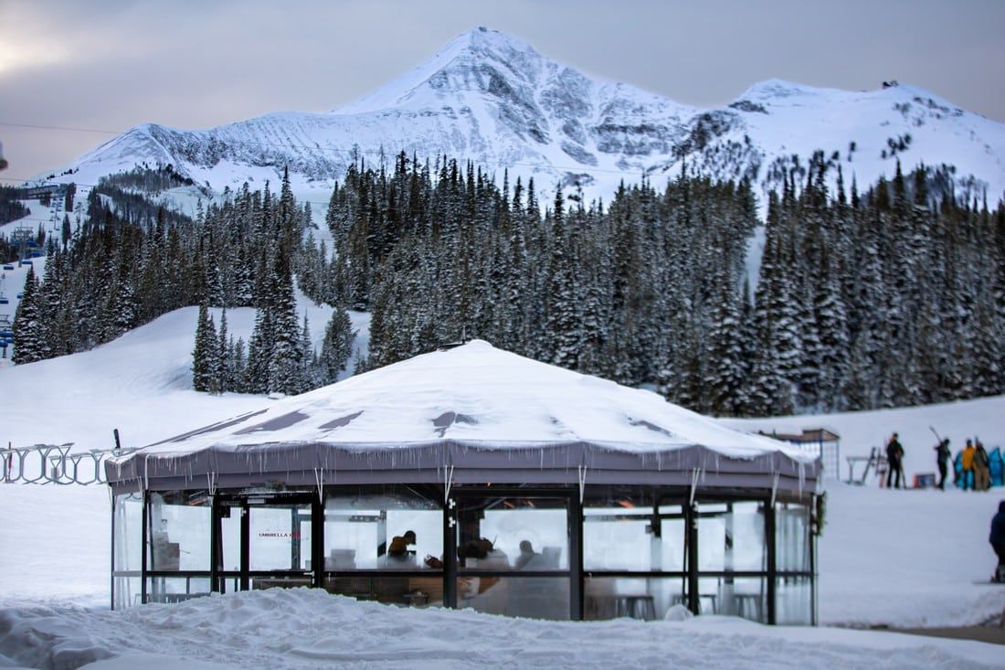 A gazebo covered in snow with a mountain in the background.