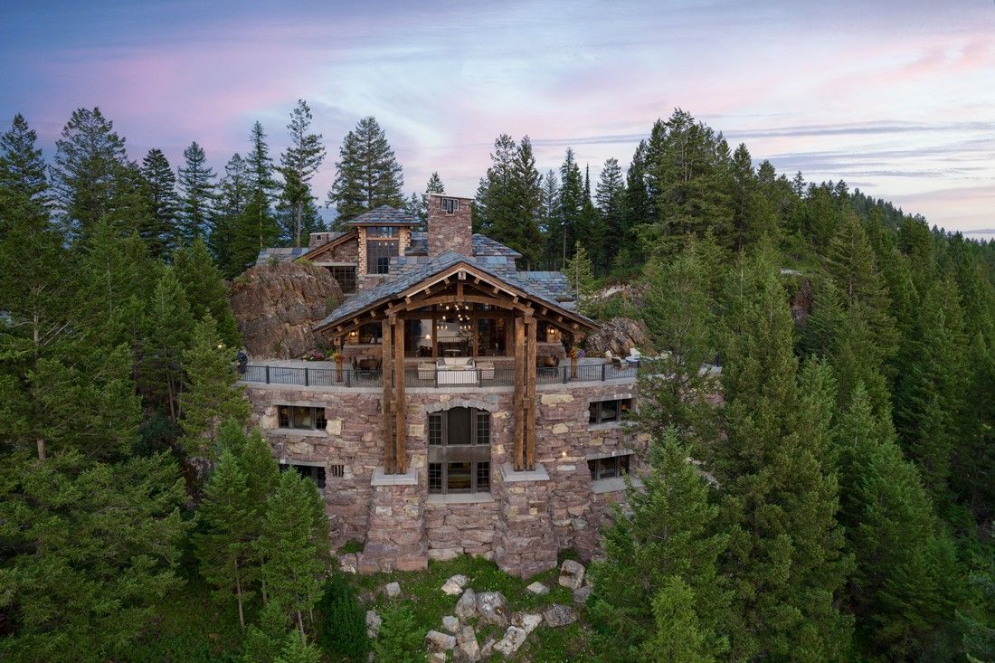 An aerial view of a large stone house in the middle of a forest.
