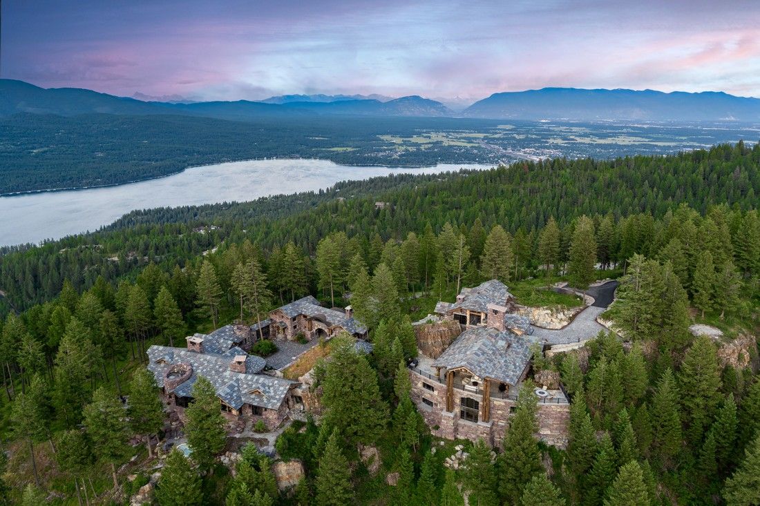 An aerial view of a large house in the middle of a forest.