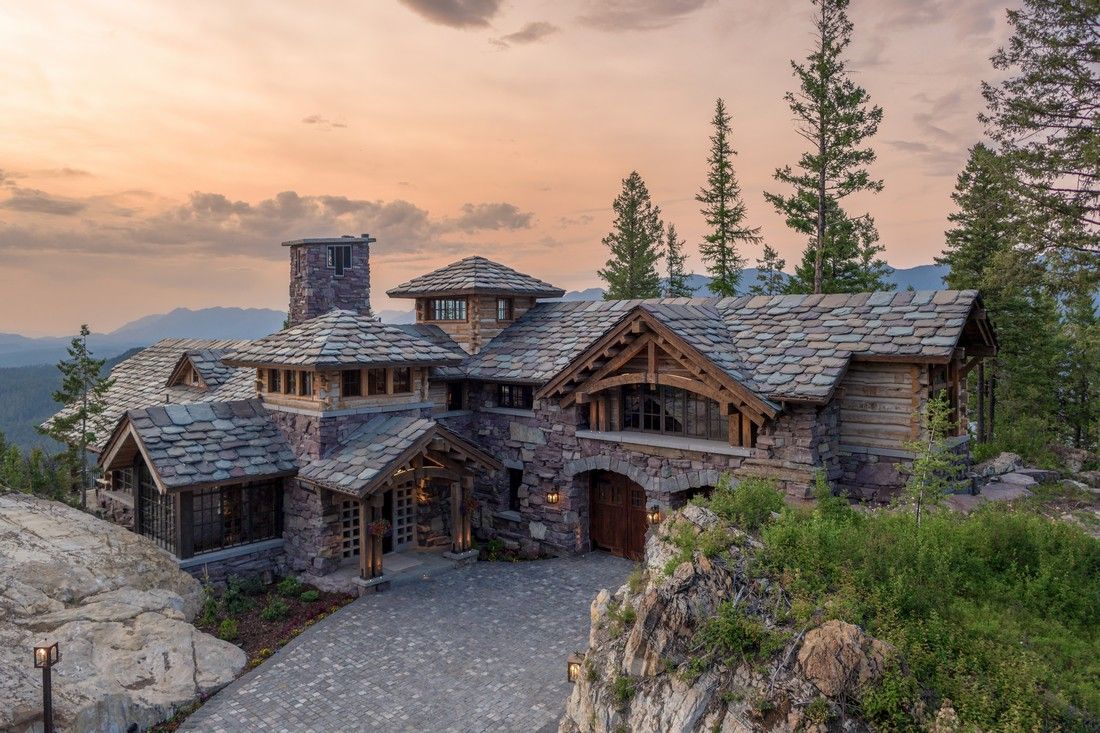 A large stone house is sitting on top of a rocky hill surrounded by trees.