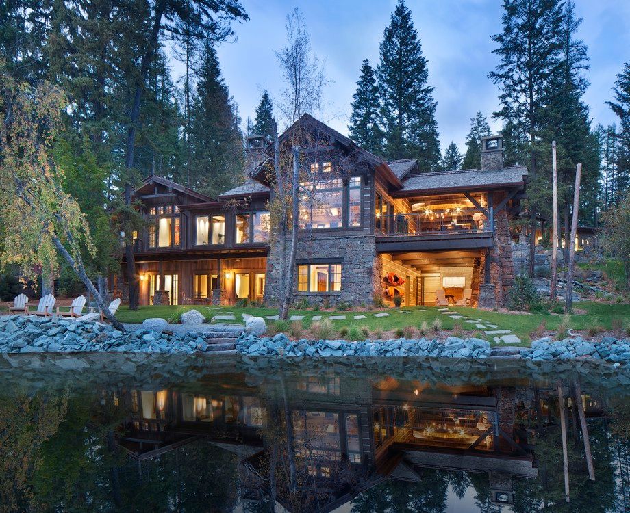 A large house sits on the shore of a lake surrounded by trees