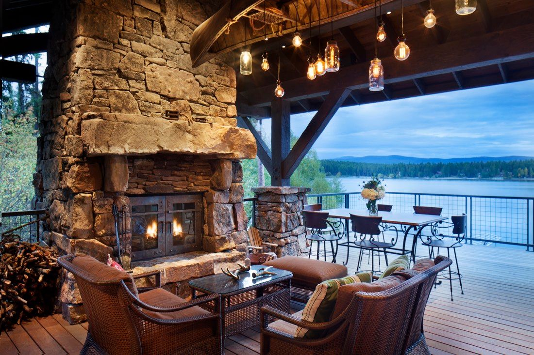 A patio with a fireplace and chairs overlooking a lake