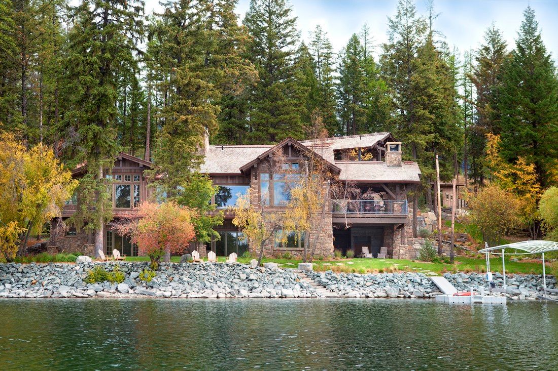 A large house is sitting on the shore of a lake surrounded by trees.