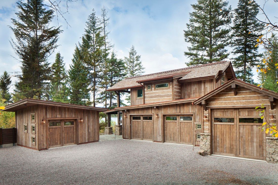 A large wooden house with three garage doors is surrounded by trees.