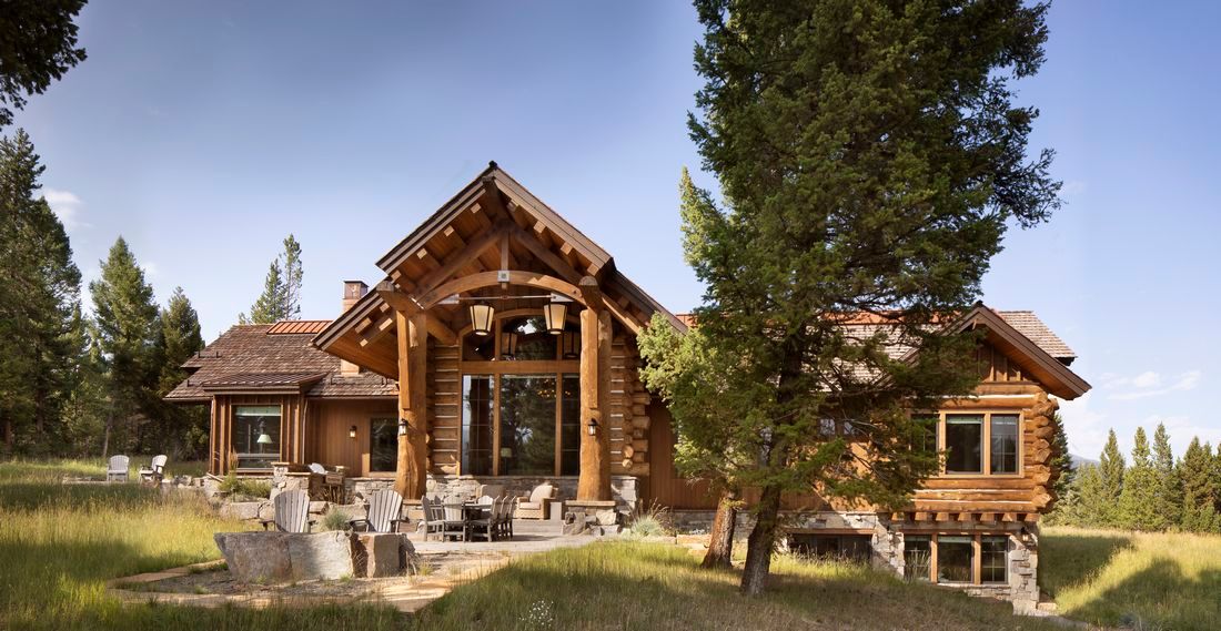 A large log cabin is sitting in the middle of a grassy field surrounded by trees.