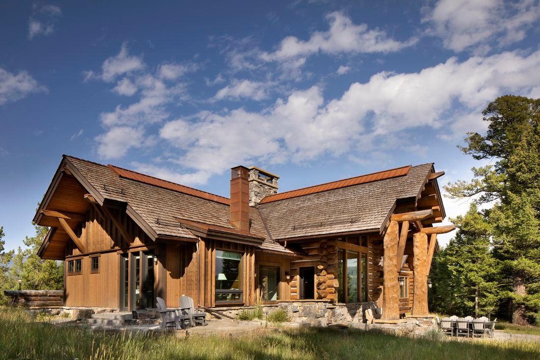 A large wooden house is sitting in the middle of a grassy field.