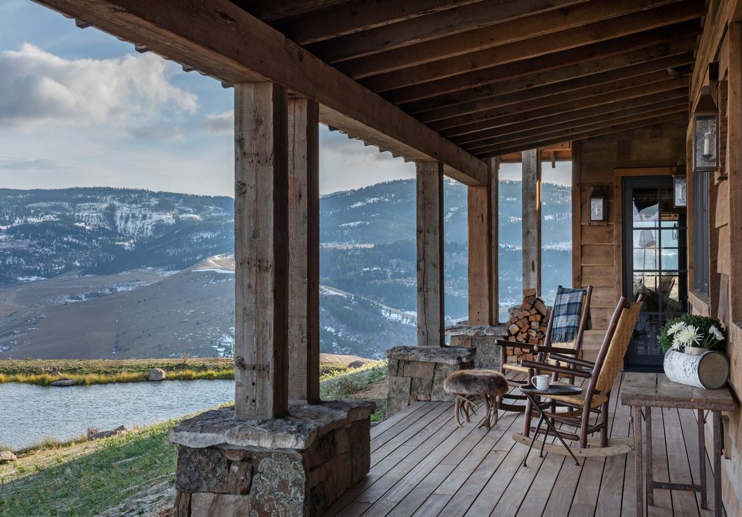 A porch with rocking chairs and a view of mountains and a lake.