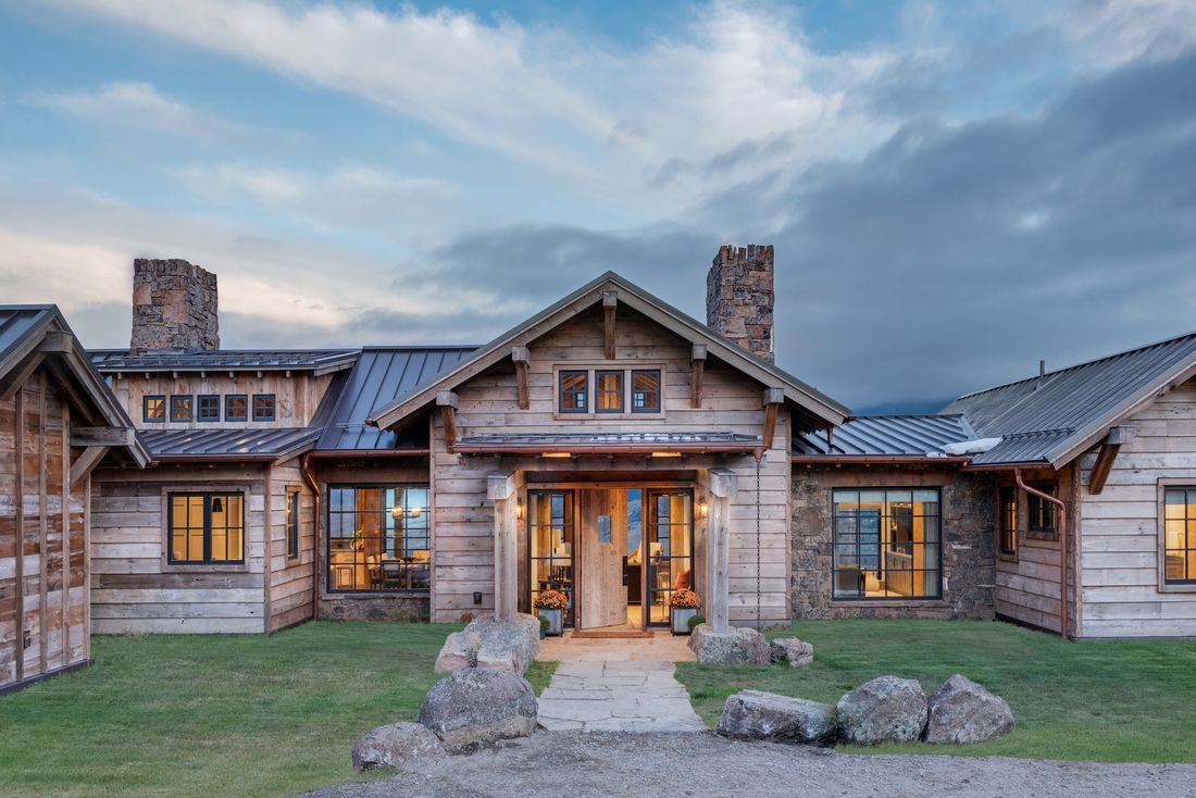 A large wooden house with a metal roof is sitting on top of a lush green field.